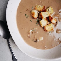 Photo d'une crème aux champignons servie dans une assiette avec des croûtons et du thym.