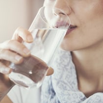 Une femme boit un grand verre d'eau.