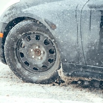 Gros plan sur le côté d'une voiture et un pneu qui roule sur une chaussée enneigée durant une tempête de neige.