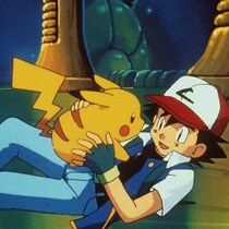 Couché par terre, Ash tient Pikachu dans ses mains en souriant.