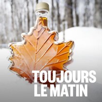 Une bouteille de sirop dans un boisé posée sur la neige.