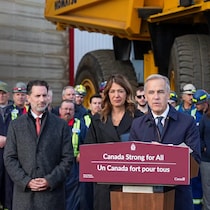 Mark Carney parle au lutrin en compagnie de la première ministre de l'Alberta, Danielle Smith, devant un mur de travailleurs et un camion pétrolier.