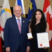 Le lieutenant-gouverneur et Elle Peters debout l'un à côté de l'autre. Elle Peters tient un certificat d'une main et une médaille de l'autre.