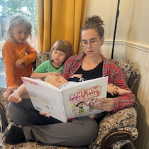 Geneviève Latour, assise avec ses trois enfants, lit un gros livre.