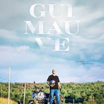 Daniel Grenier est devant une moto sur la route. Guimauve est écrit dans le ciel. 