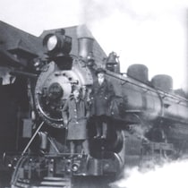Une image ancienne d'un train avec deux personnes sur la locomotive.