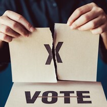 Une personne qui tient un bulletin de vote déchiré en deux parties.