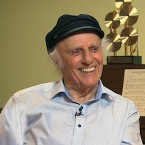 Gilles Vigneault en entrevue chez lui, en novembre 2017, à 89 ans. Il porte une casquette et est assis au piano.