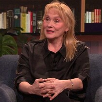 Une femme sur un plateau de télévision. Elle est assise dans un fauteuil.