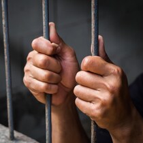 Gros plan sur des mains qui tiennent des barreaux de prison.