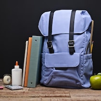 Un sac d'école est déposé sur un table. Autour, il y a une pomme, un cartable, des cahiers, de la colle, une efface, une calculatrice et du ruban d'adhésif. 