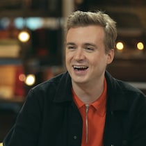 Il est invité sur le plateau de l'émission Pire du pire et rigole, assis.