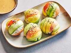 Des boules de riz à sushi garnies de tranches de légumes servies avec de la sauce au sésame.