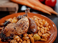 Une assiette contenant des haricots, une saucisse et du poulet.