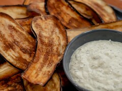 Des chips d'aubergines dans une assiette avec un bol rempli de tzatziki au labneh.