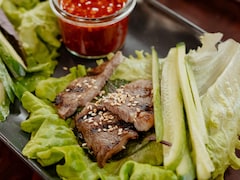 Des côtes de bœuf kalbi dans une assiette avec des lanières de concombres, de la laitue et un bol de sauce.