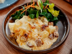 Une portion de gratin de pommes de terre, chou-fleur et merguez dans une assiette avec de la salade.