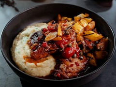 Des hauts de cuisse de poulet dans une assiette avec de la polenta et des légumes.