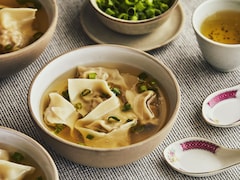 Un bol de soupe wonton avec des cuillères à soupe asiatiques et des oignons verts.