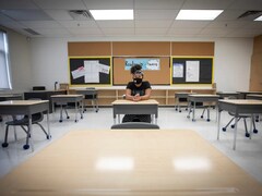 Une élève est seule dans une classe, assise à son bureau avec un masque.