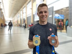 L'athlète sourit à la caméra en montrant ses deux médailles. 