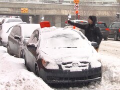 Un homme enlève la neige sur le toit d'une voiture avec une petite pelle.