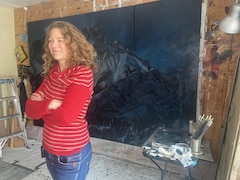 L'artiste Bigoudi debout devant une de ses toiles qui représente les Rocheuses de nuit.