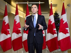M. Morneau est debout au micro devant une série de drapeaux canadiens. 
