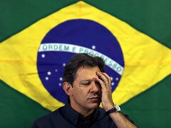 Le candidat de la gauche à la présidentielle brésilienne, Fernando Haddad, une main au visage devant un drapeau du Brésil.