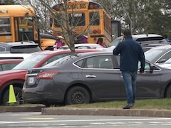 Un parent au téléphone sur un stationnement devant l'école Beaubassin. Au fond, des enfants embarquent dans des autobus scolaires.