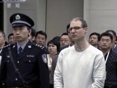 Flanqué de deux policiers chinois, un homme portant des lunettes et les cheveux très courts assiste à l'audition de son appel.