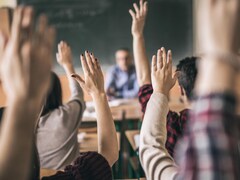 Des élèves photographiés de dos dans une classe lèvent la main