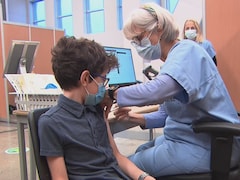 Un enfant se fait vacciner contre la COVID-19 par une infirmière en uniforme bleu.