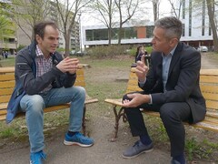 Deux hommes discutent, assis sur un banc de parc, au printemps. 