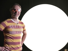 Un homme sourit avec des lunettes conçues pour regarder une éclipse devant un grand ballon illuminé.