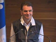 François Bonnardel pendant une conférence de presse. Il y a un drapeau du Québec derrière lui. 