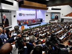 Des journalistes filment et photographient une salle remplie de dignitaires. 