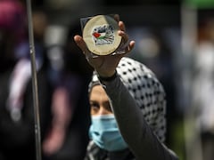 Une manifestante masquée tient dans sa main levée un message: Libérez la Palestine.  