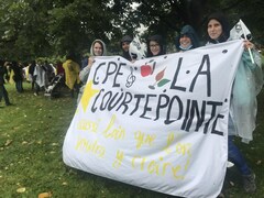 Quatre éducatrices en CPE tiennent une banderole où on peut lire : CPE la Courtepointe, aussi loin que l'on voudra y croire.
