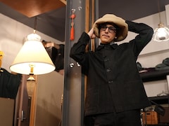 Hubert Lenoir porte un chapeau beige et une grande chemise noire dans un studio d'enregistrement. 
