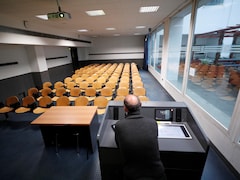 Un professeur est vu de dos devant une classe vide.