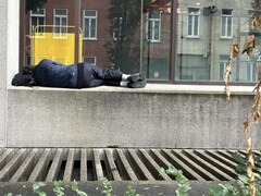 Un homme dort sur un muret de béton, le long d'un immeuble.