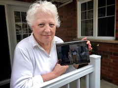 Une dame tient dans ses mains une tablette où elle montre une photo de son fils et de sa bru. 