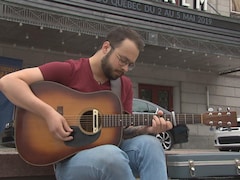 Jeffrey Piton avec sa guitare sur les marches devant le Palais Montcalm à Québec