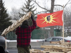 Un homme transporte une palette de bois, un drapeau mohawk flotte tout près.