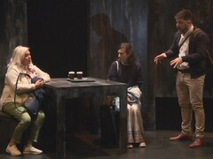 Trois acteurs sur scène dont deux femmes sont assises autour d'une table.