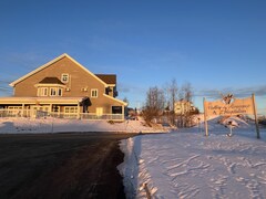 Une maison éclairée par le coucher du soleil avec plein de neige sur let errain. 