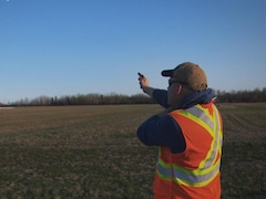 Un homme portant un dossard debout dans un champ avec un fusil dans les mains.