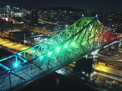 Une vue aérienne et de nuit du pont Jacques-Cartier illuminé, avec en arrière plan le centre-ville de Montréal.