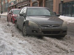 Trois voitures obstruent une partie de la rue puisqu'elles ne peuvent pas se garer près des trottoirs en raison de la neige. 